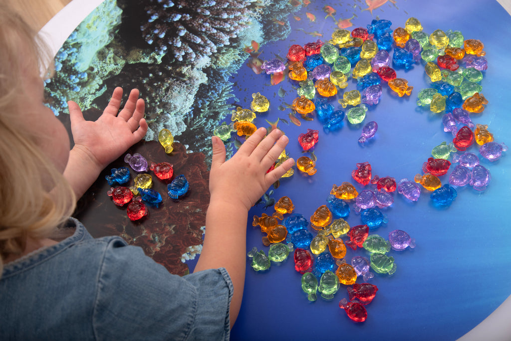 Translucent color fish set: hands arranging multicolor fish on a blue tray