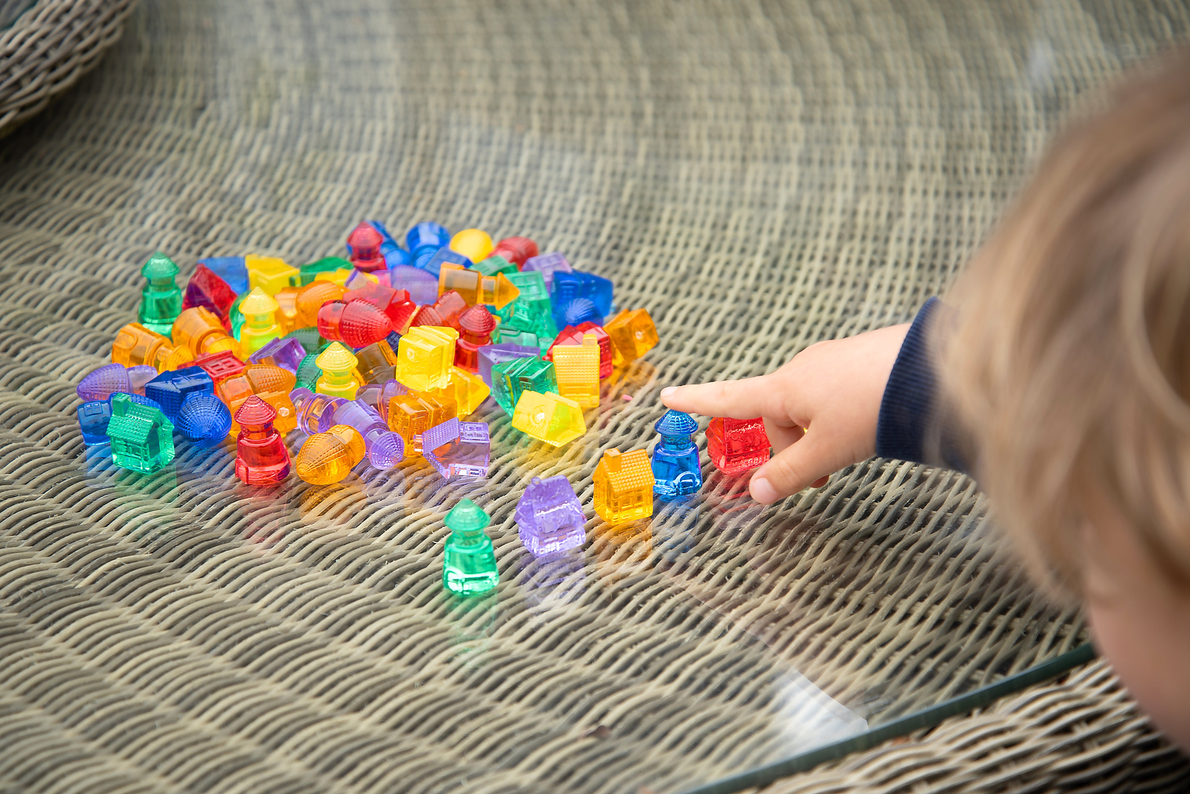 Hand reaching into pile of translucent colored toy houses on woven table