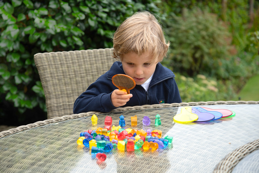 Child playing with translucent colored toy houses on outdoor table