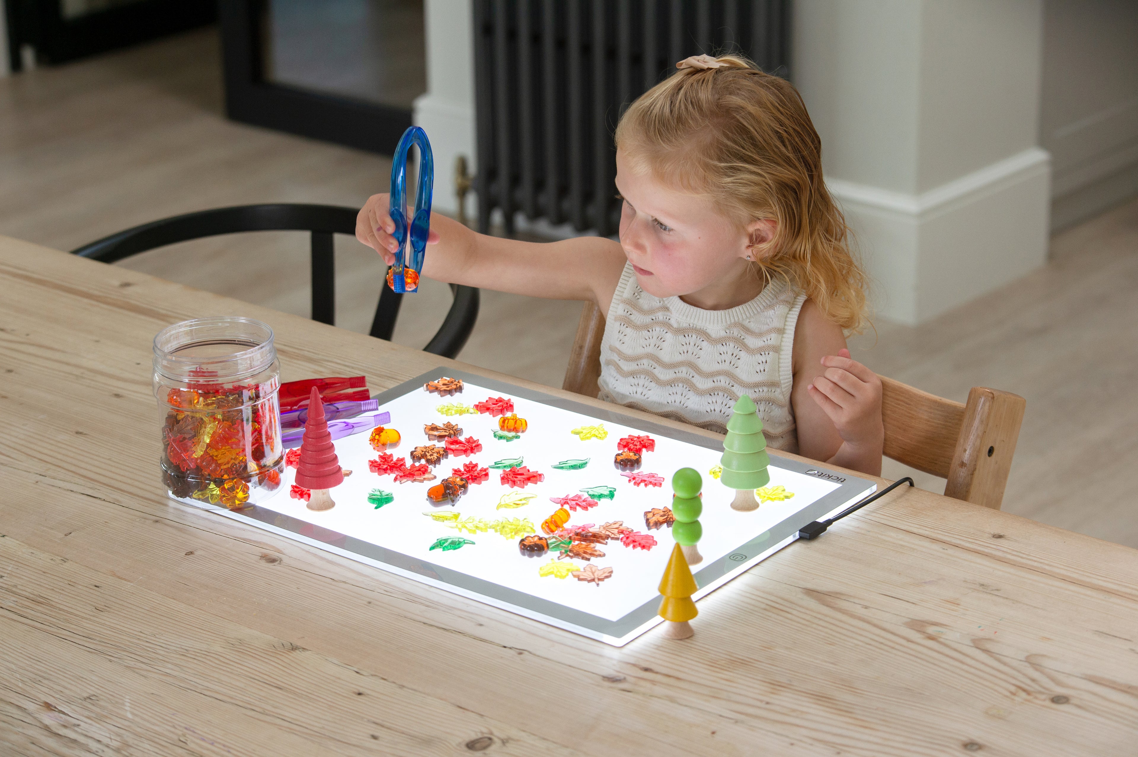 Child reaching toward translucent leaf and seed craft pieces on a light tray