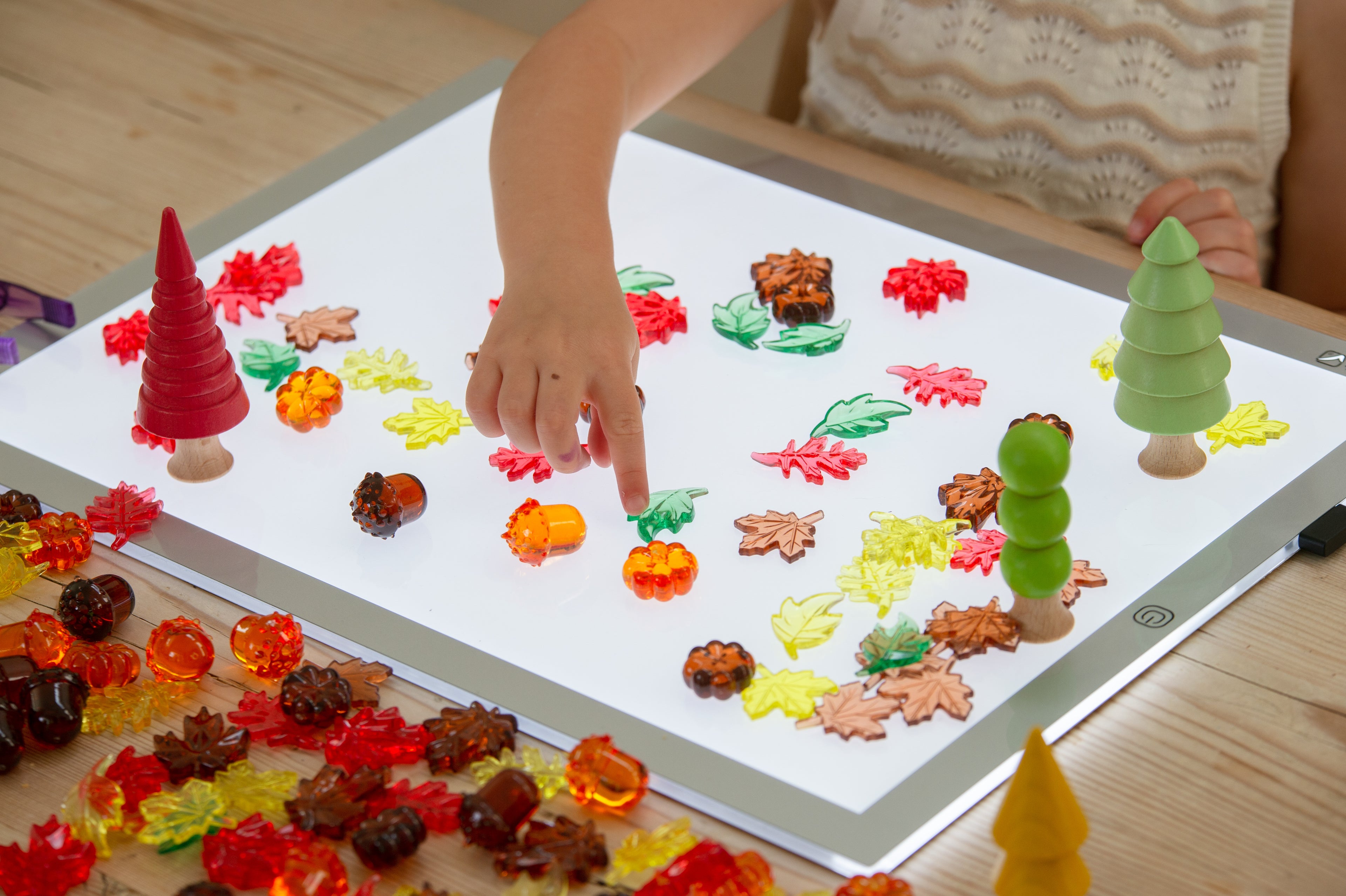 Child arranging translucent leaf and seed craft pieces on a light tray