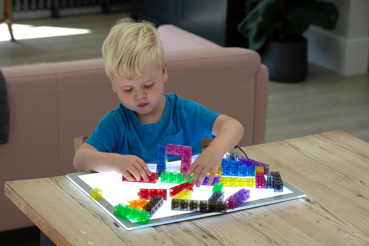 Child arranging translucent linking cubes on a clear tray, colorful connected pieces