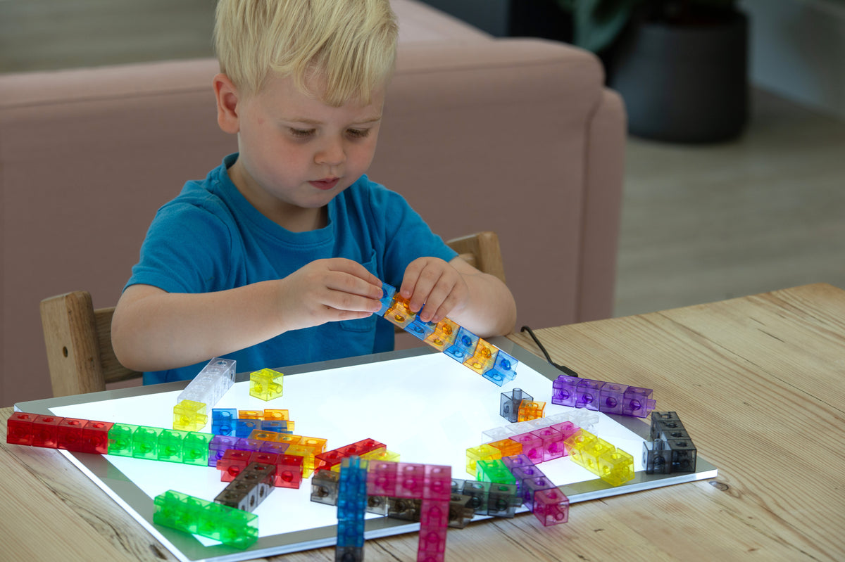 Child building with translucent linking cubes on a clear tray, multicolor rods