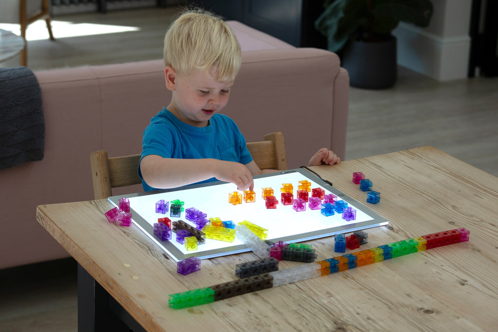 Child playing with translucent linking cubes, colorful pieces on a clear tray