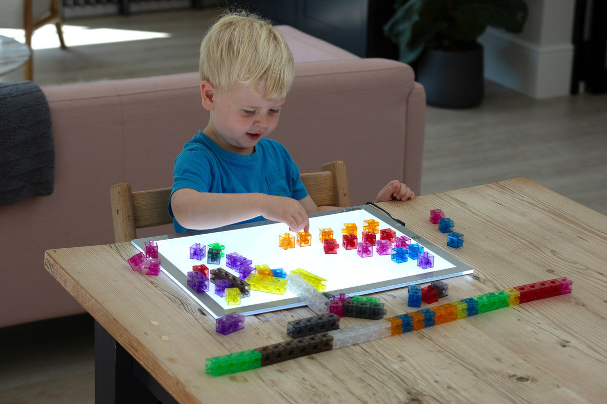 Child playing with translucent linking cubes, colorful pieces on a clear tray