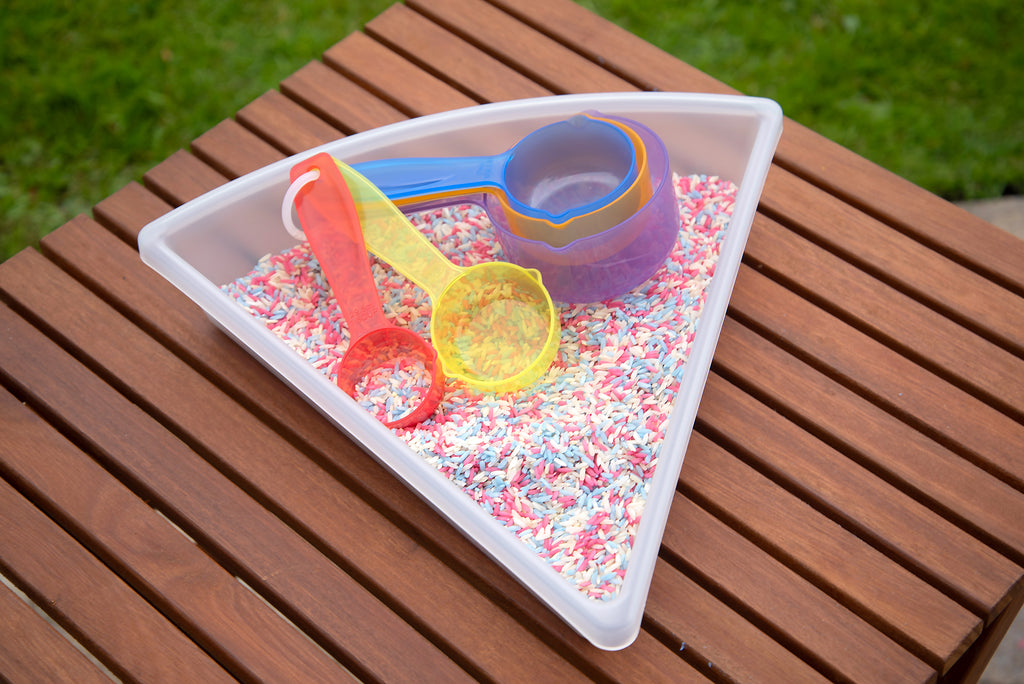 Translucent measuring cups in a triangle tray with colorful sprinkles, orange, blue, and yellow