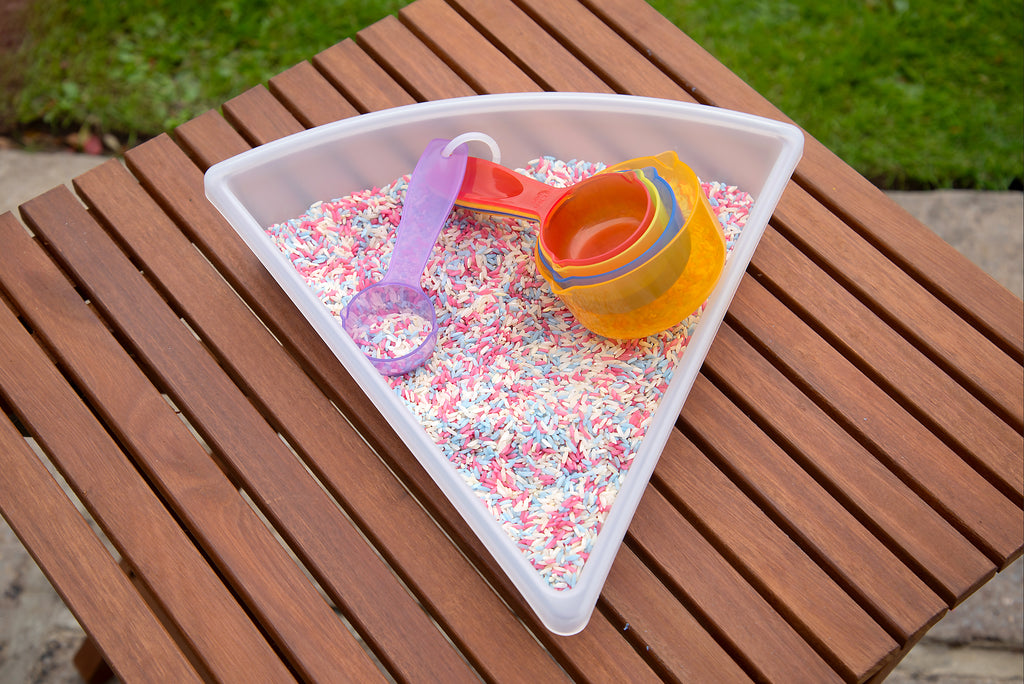 Translucent measuring cups in a tray with colorful sprinkles, stacked red and orange bowls