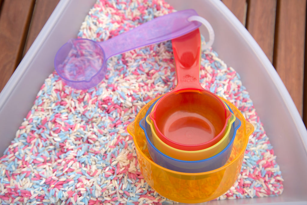 Translucent stackable measuring cups with pink, orange, and purple bowls on colorful sprinkles