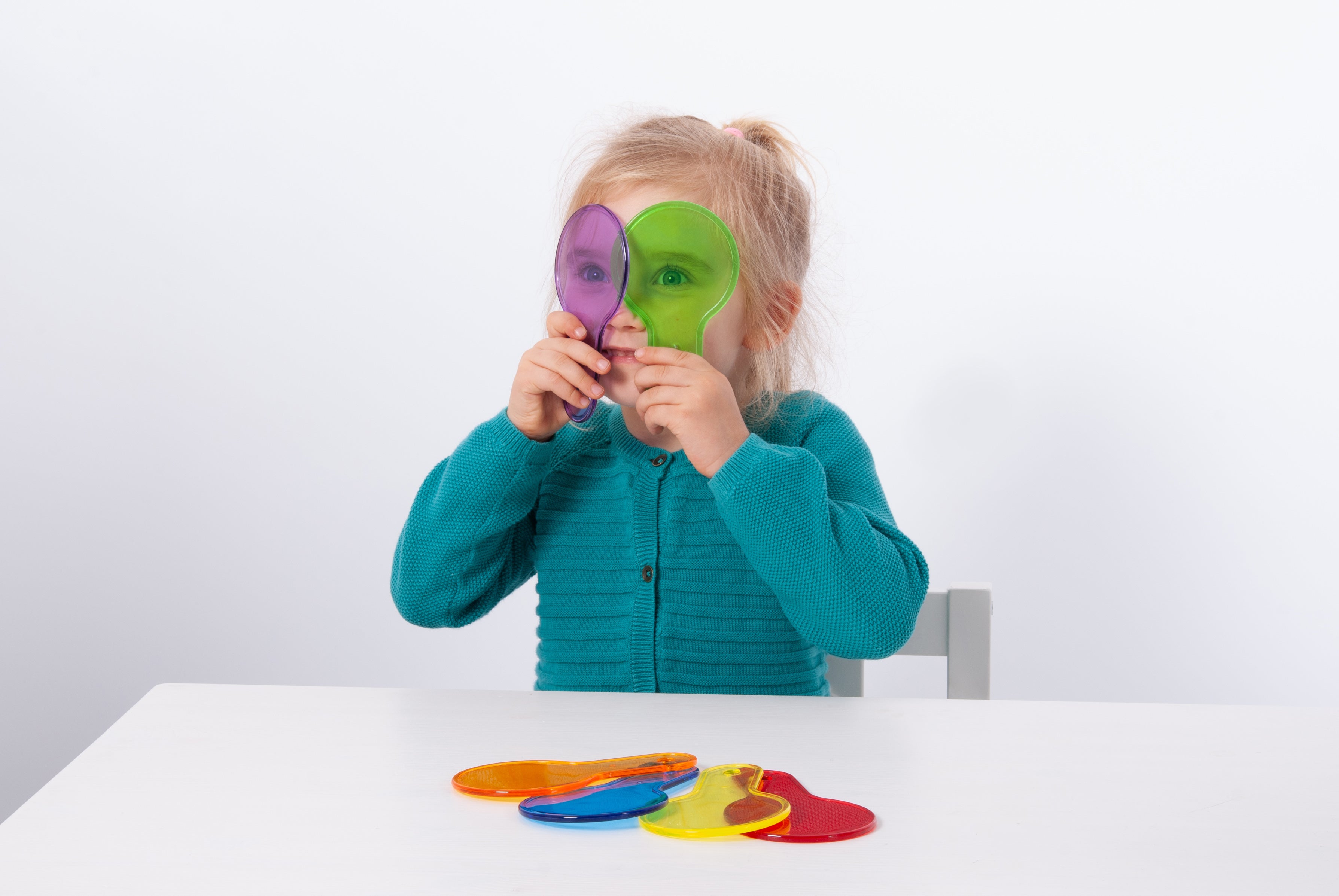 Translucent color paddle toys with handles; child holds purple and green paddles up near eyes.
