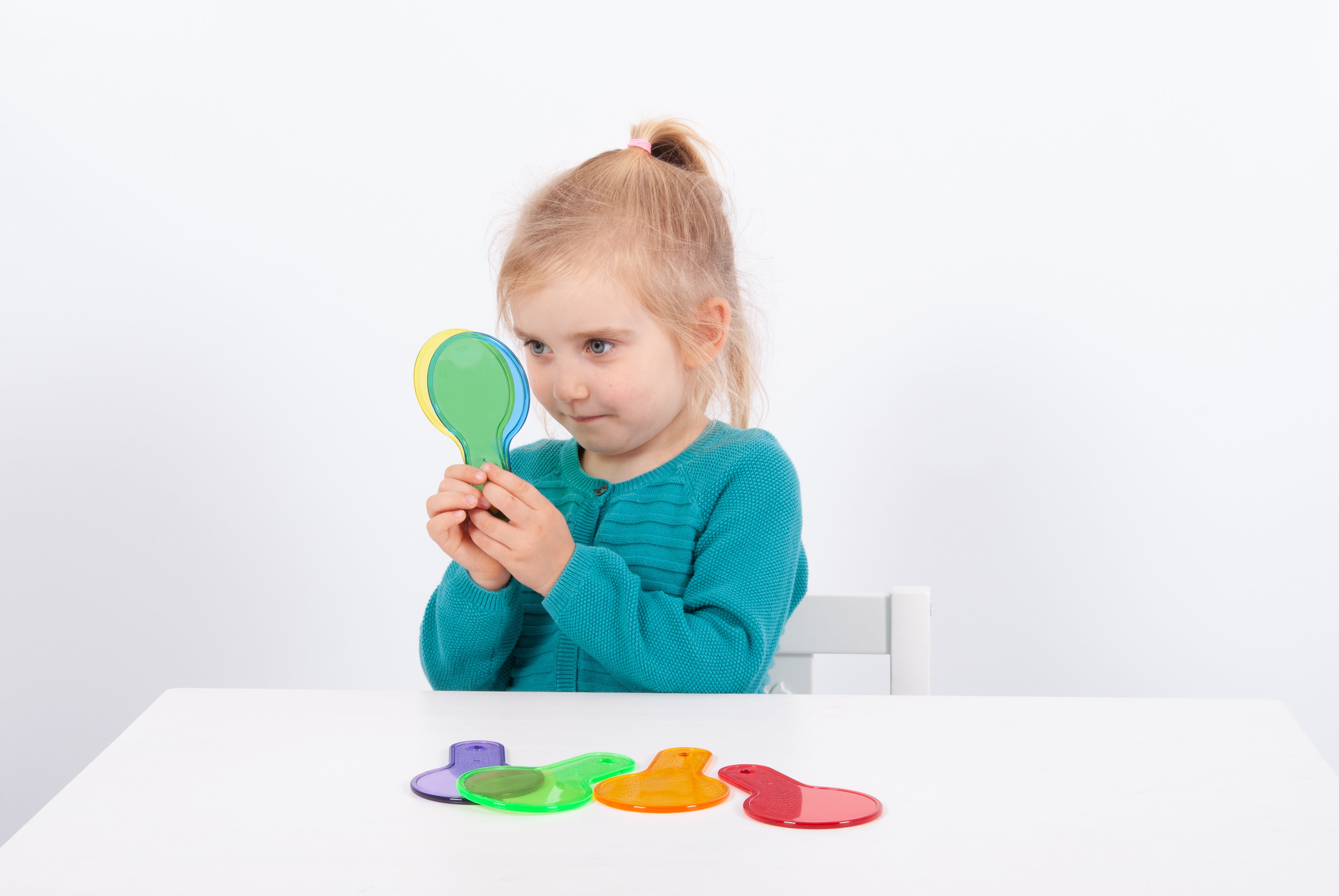 Translucent paddle toy with handle; child holds green paddle, other colorful paddles on table.