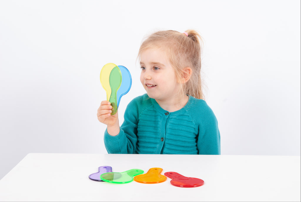 Translucent paddle toy with handle; child holds green-blue paddle while others rest on table.