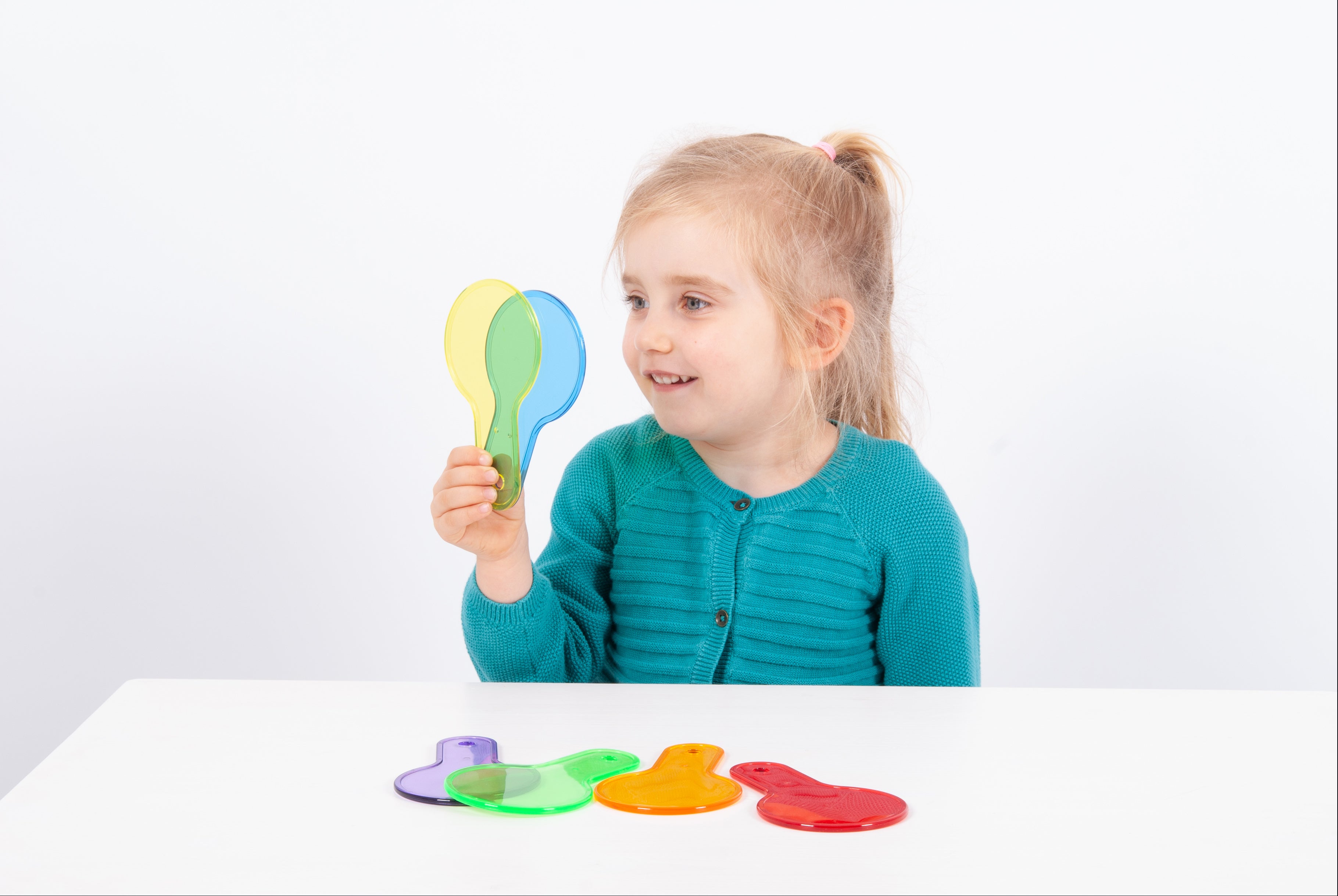 Translucent paddle toy with handle; child holds green-blue paddle while others rest on table.