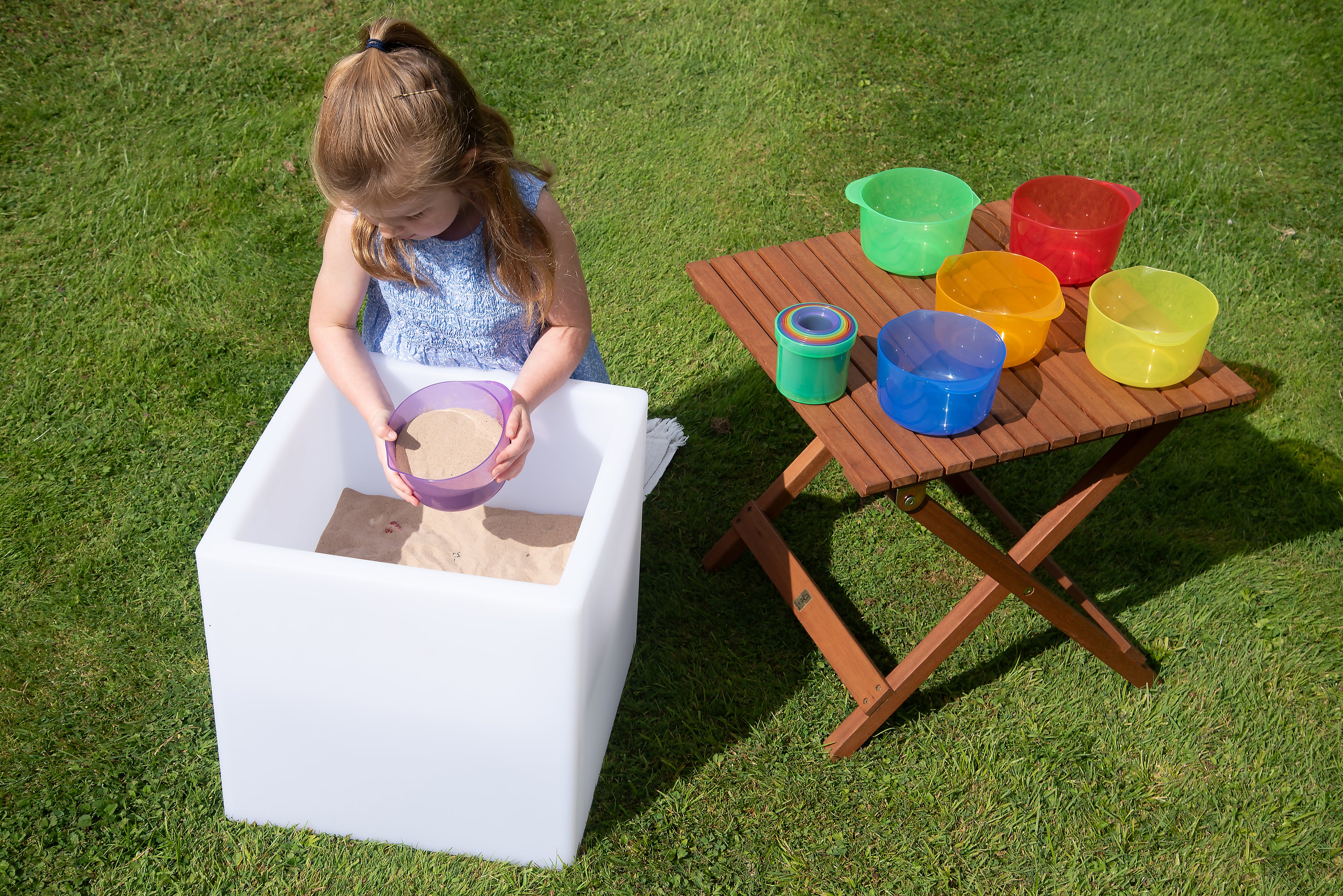 Child with translucent pouring bowls on wooden table in green, red, blue, orange, and yellow