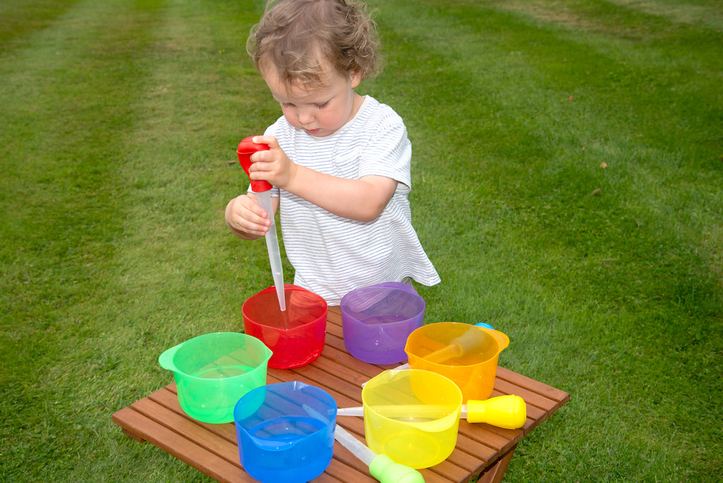 Child holding a translucent red pouring bowl, with purple, green, blue, and yellow bowls