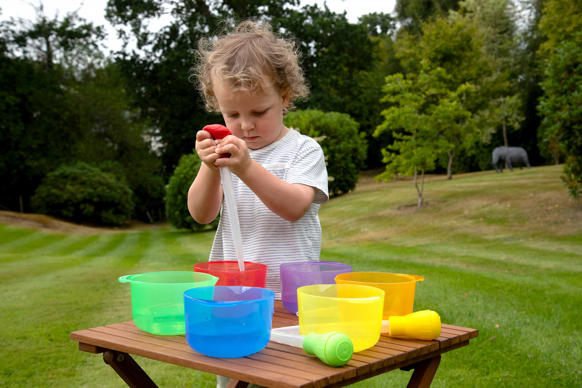 Child pouring into a translucent red cup-style bowl, with green, blue, yellow, and purple bowls