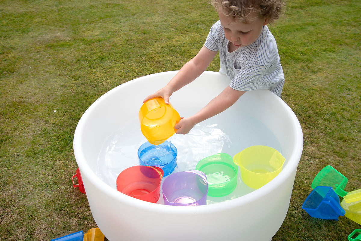 Child adds liquid to translucent yellow and blue pouring bowls in a large tub