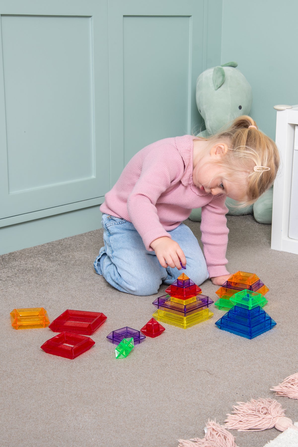 Child kneeling with translucent rainbow pyramid blocks on carpet