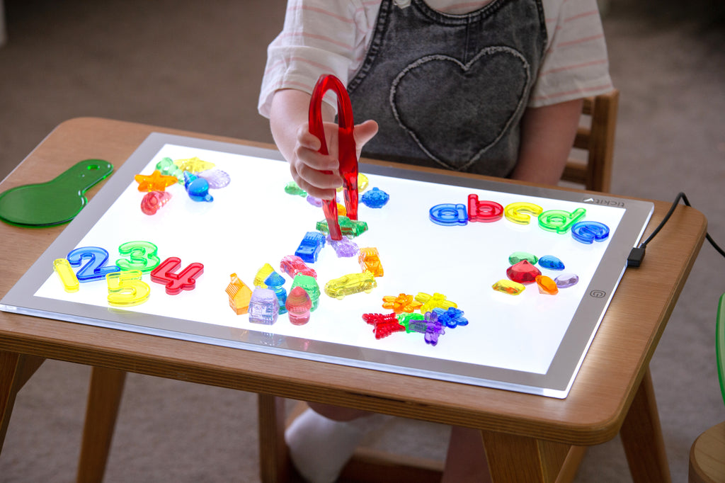 Colorful number and letter pieces on a tablet, with red scoops and bin