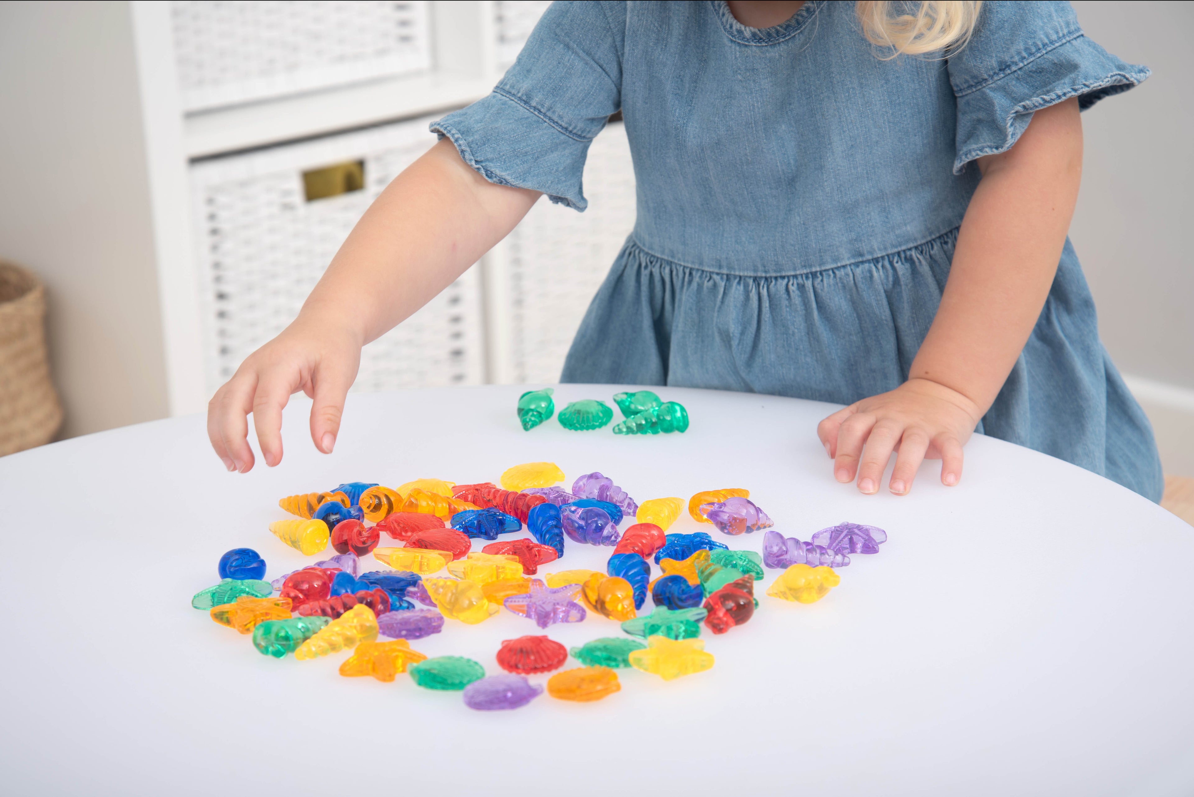 Translucent color shells with child holding green pieces over scattered multicolor shells