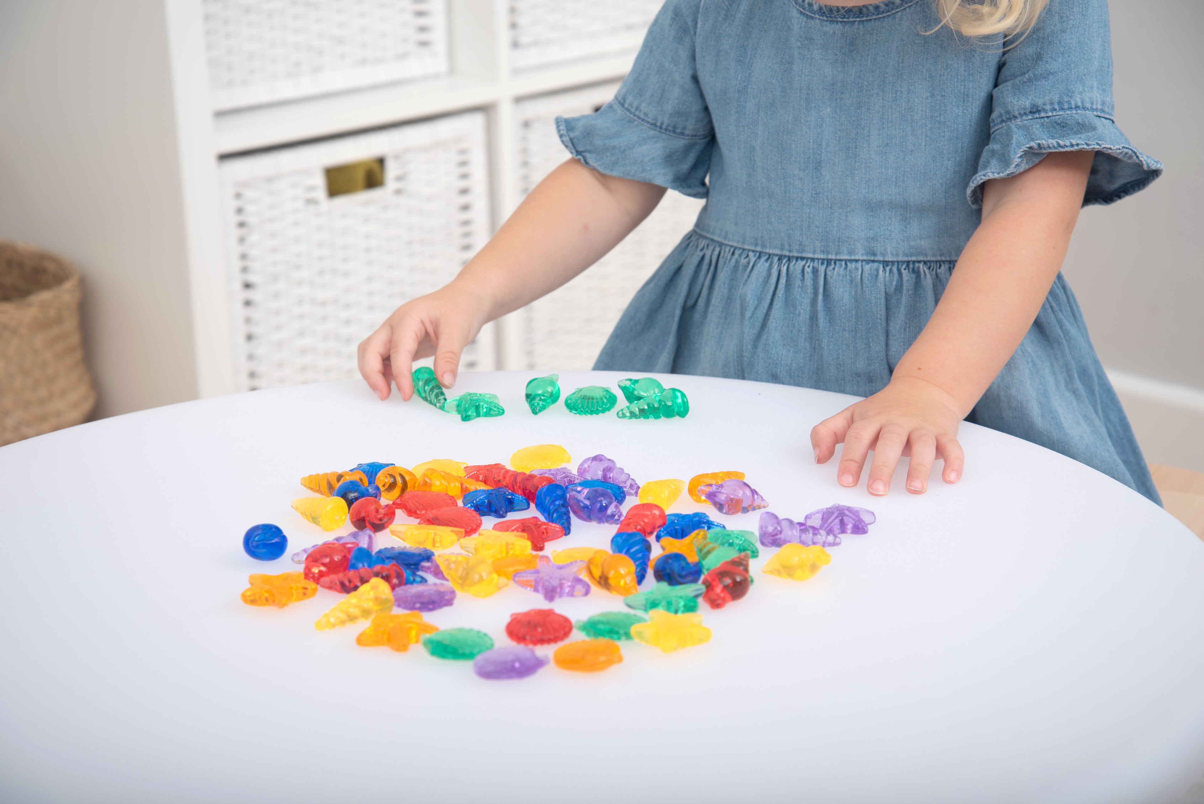 Translucent color shells set on white table, child holding green pieces and pointing
