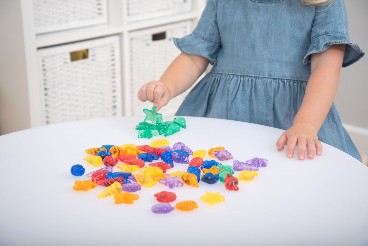 Translucent color shells set: child hand picking up green shell pieces from pile