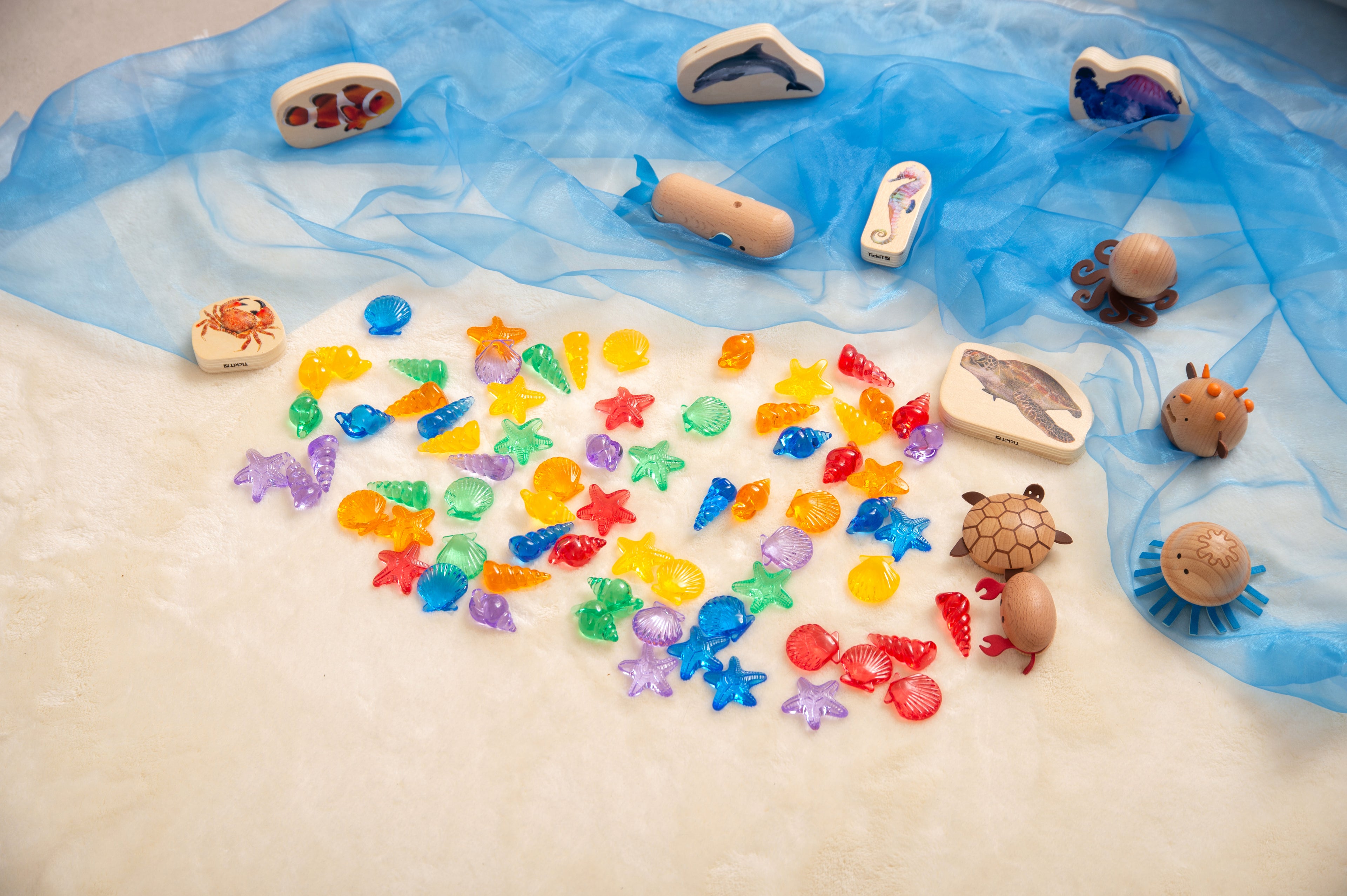 Translucent color shells scattered on blue play mat with animal-shaped sea toys