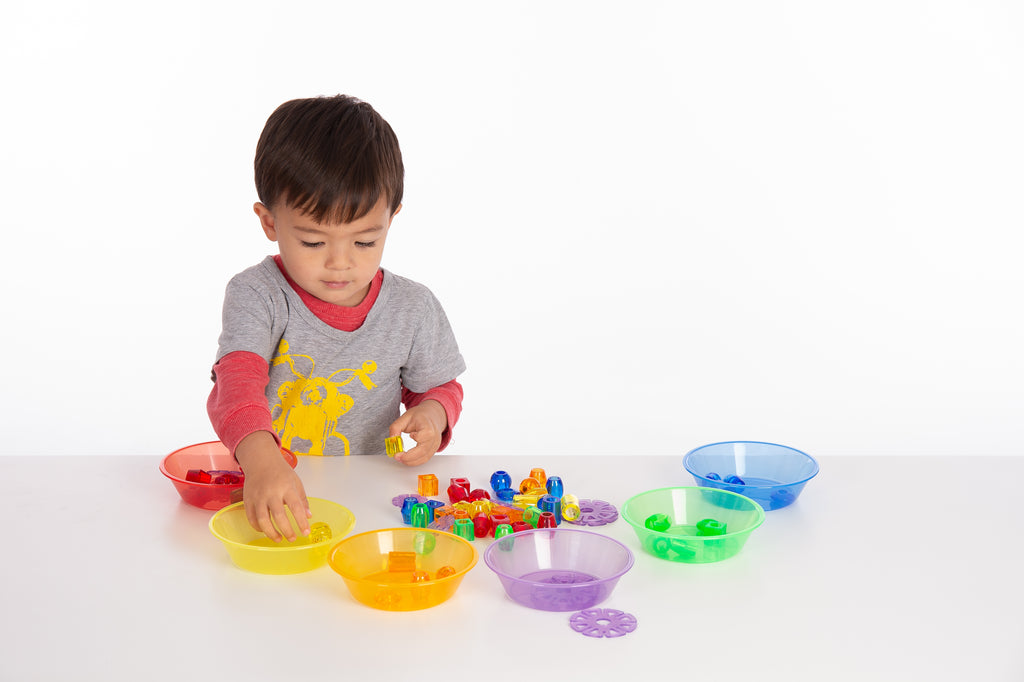 Child placing colored pieces into translucent multi-color sorting bowls