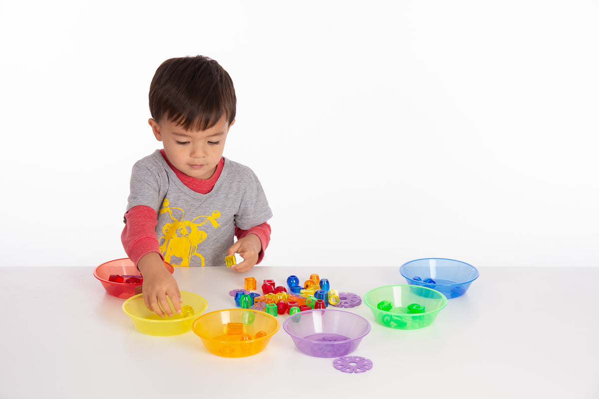 Child placing colored pieces into translucent multi-color sorting bowls