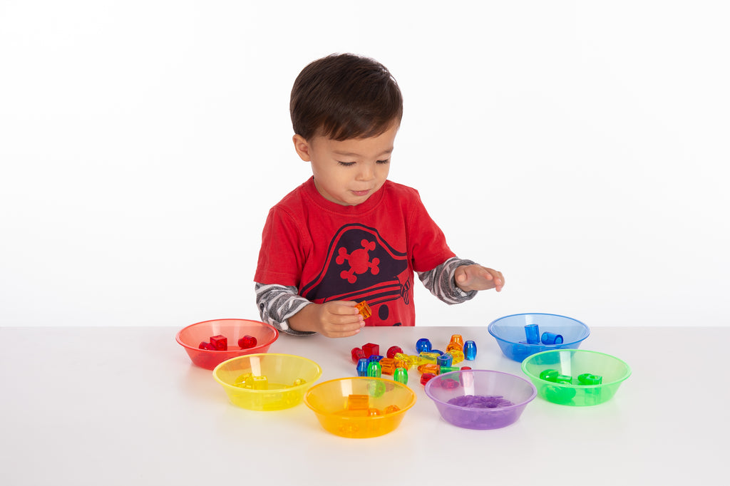 Child hands playing with translucent color sorting bowls and colorful building pieces