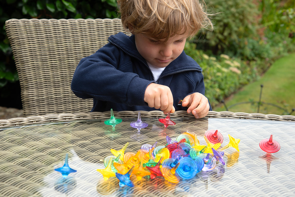 Child arranging translucent color spinners on a wicker surface