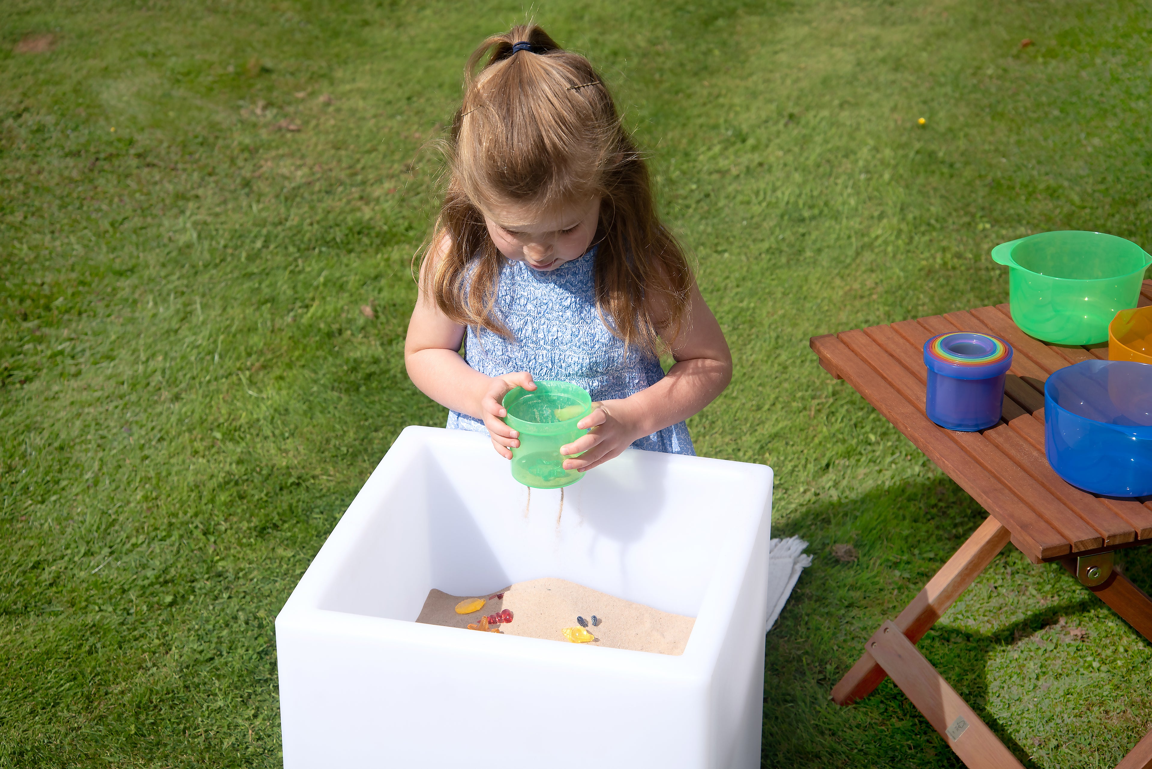Child using translucent stacking cups, pouring into a green cup outdoors.