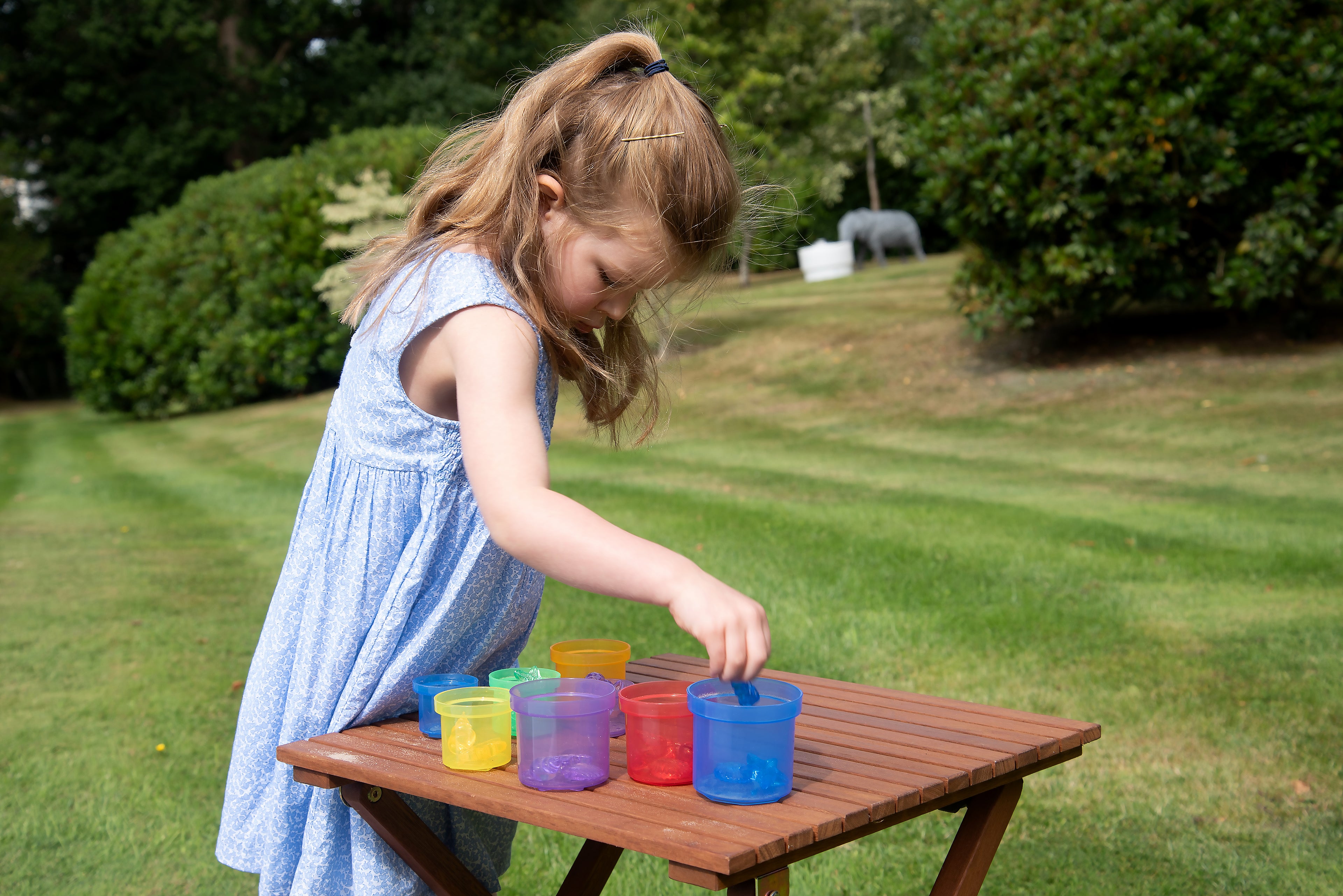 Child arranging translucent stacking cups in assorted colors on a wooden table.