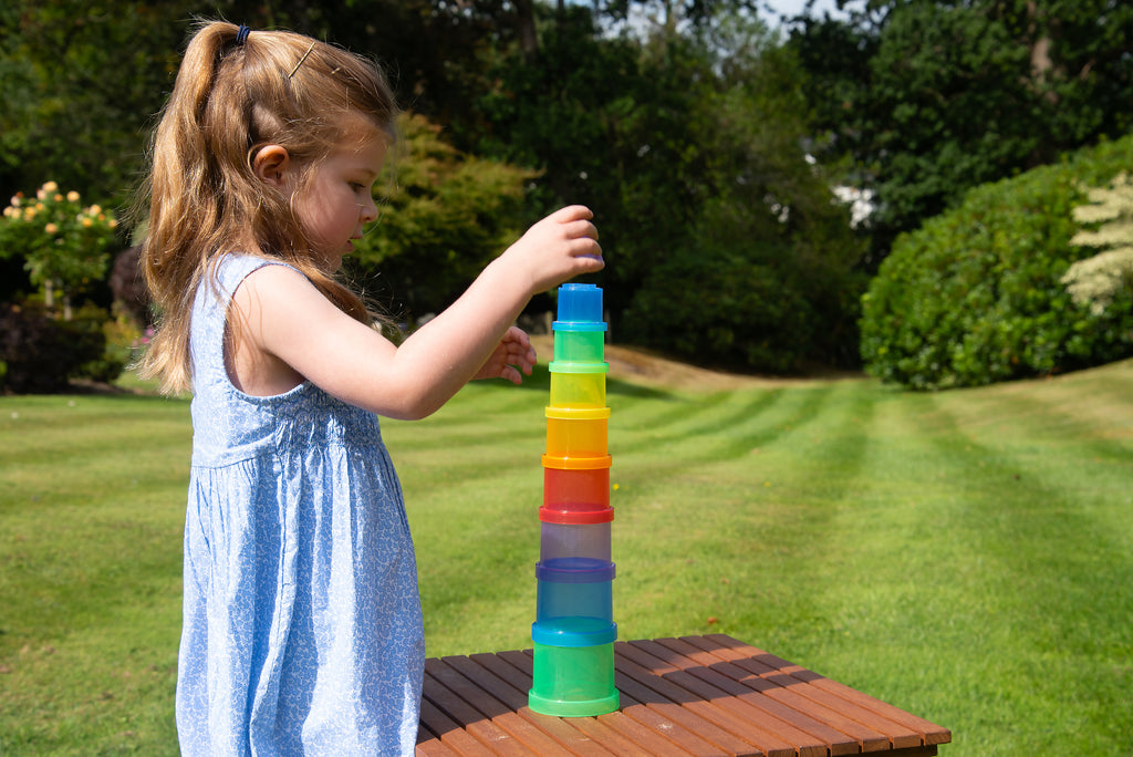 Child stacking translucent cups in a tall multi-color tower on a table.