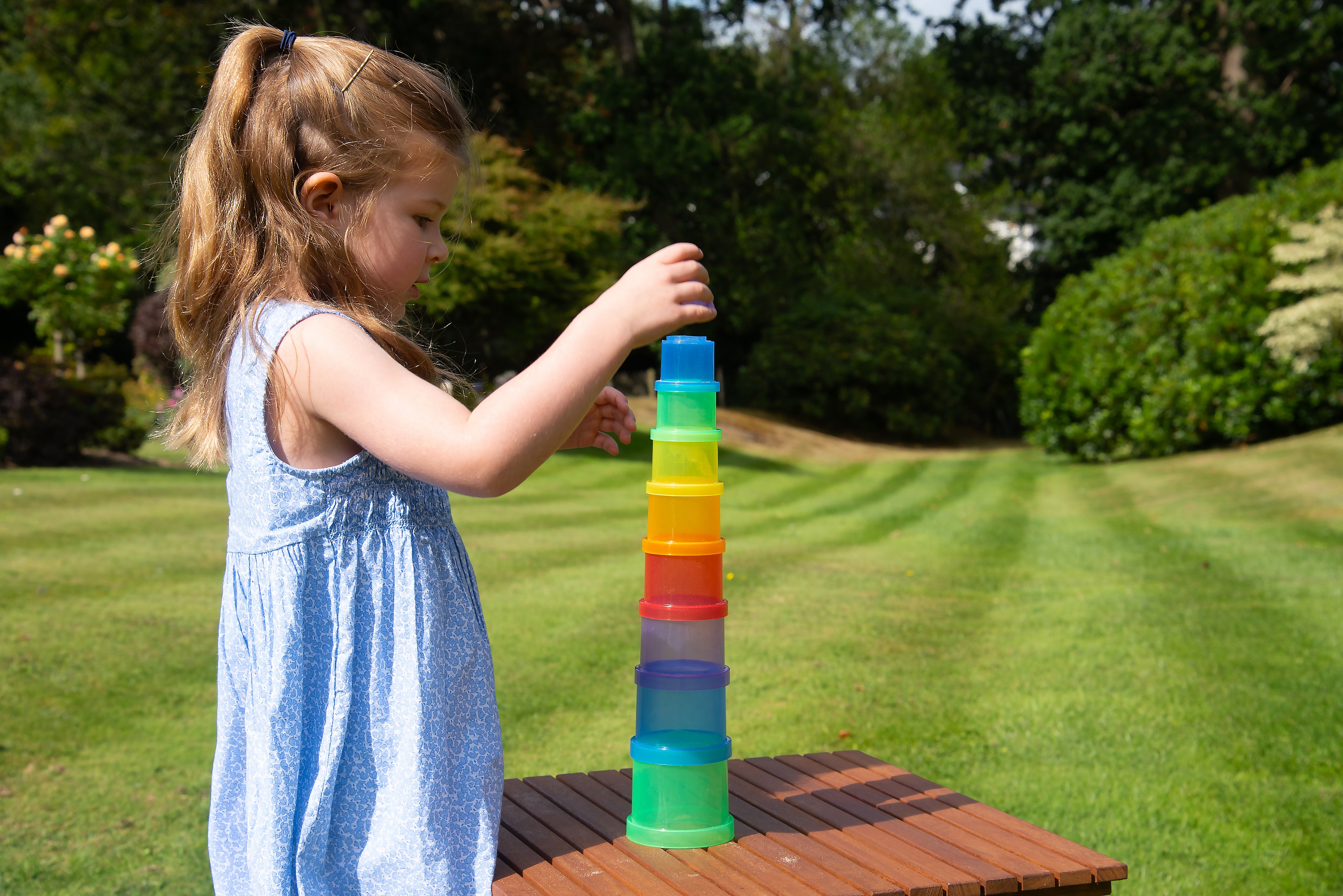 Child stacking translucent cups in a tall multi-color tower on a table.