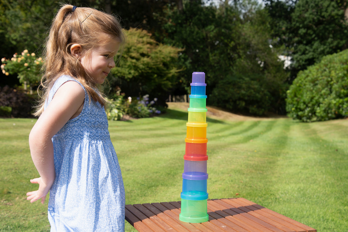 Translucent stacking cups tower with multi-color cups on a table, handled by a child.