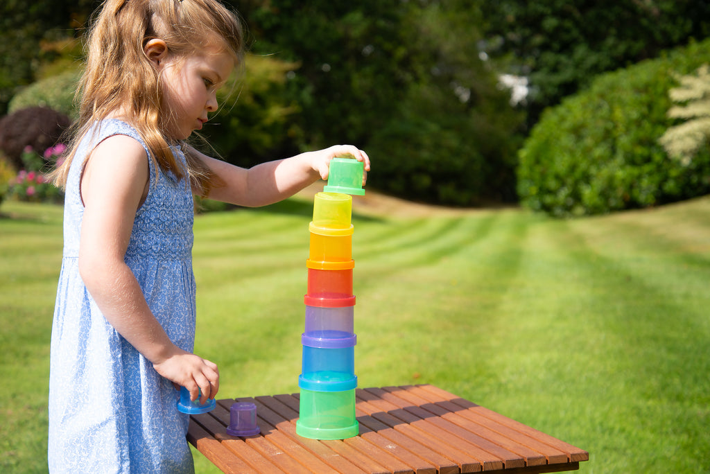 Child building a translucent stacking cups tower with multi-color cups on a table.