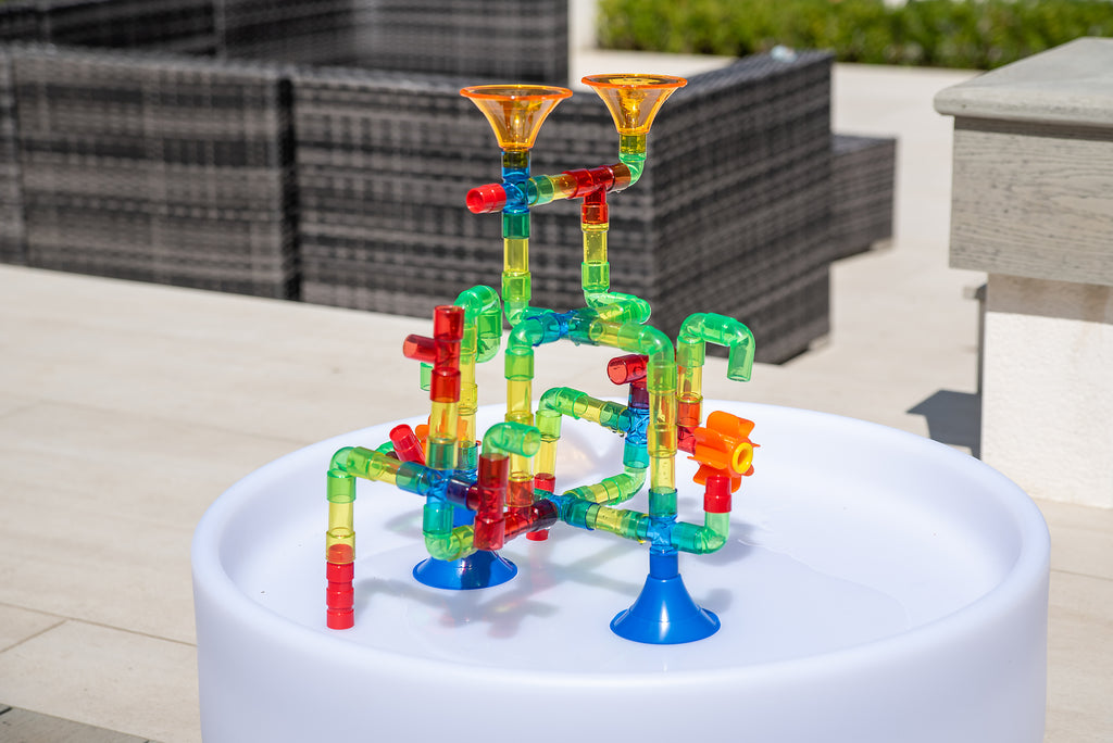 Translucent water pipe toy on a white basin with orange funnels and green tubing