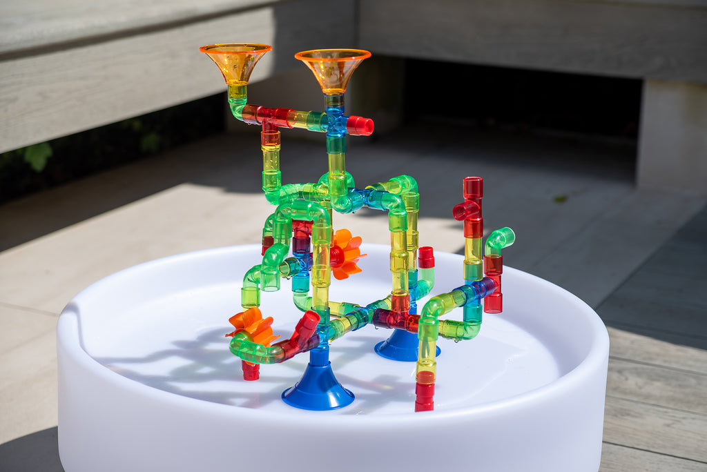 Translucent water pipe toy in a white basin with green and red tubes and orange funnels