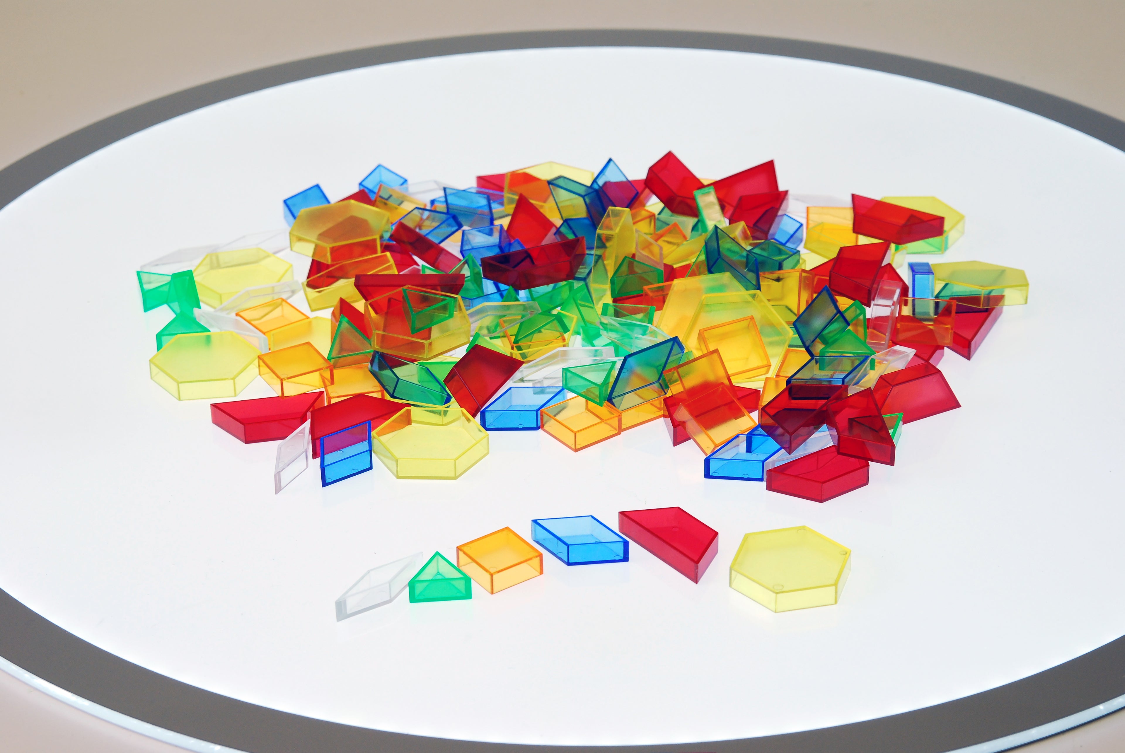 Translucent hollow pattern blocks scattered on a white circular tray, blue red green yellow