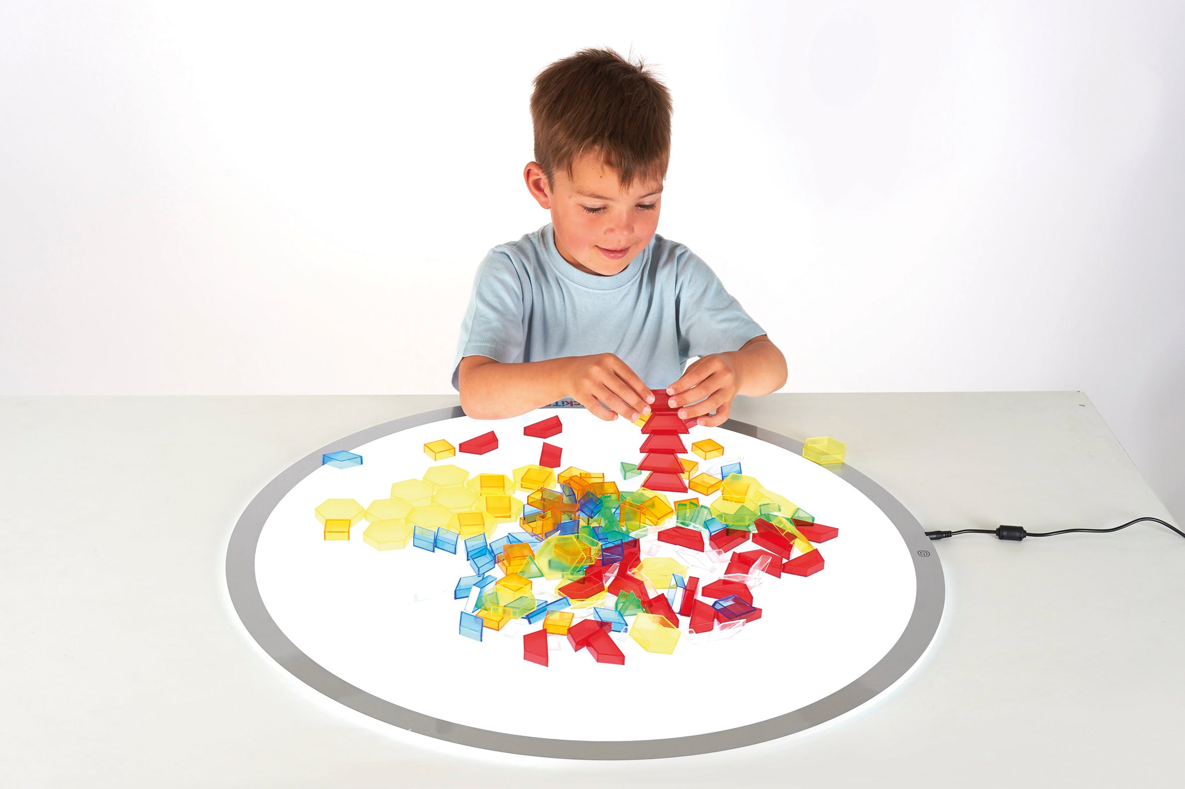 Translucent hollow blocks in mixed colors, child building on a round play mat
