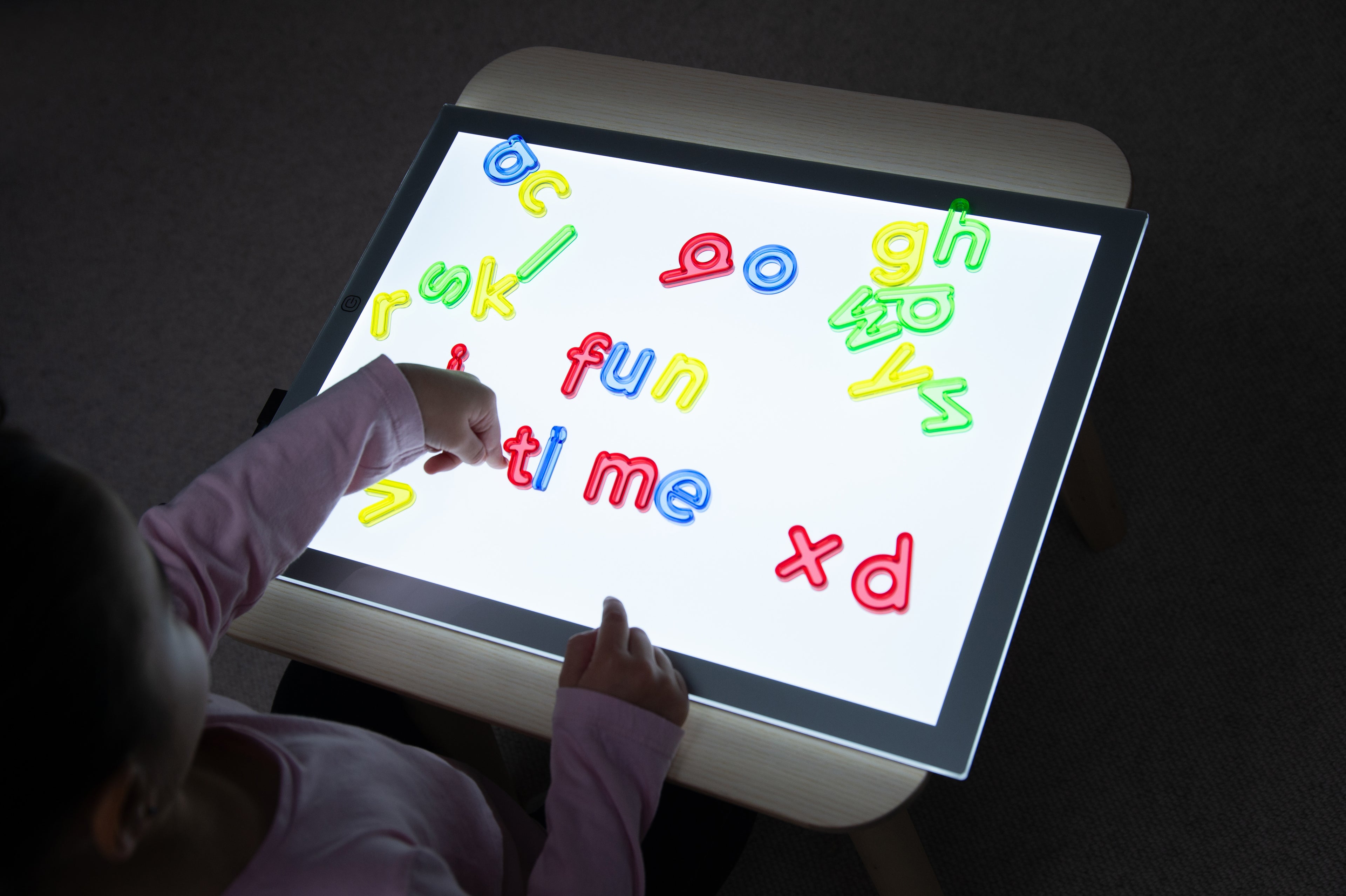 Translucent lowercase letters displayed on tablet, multicolor plastic pieces
