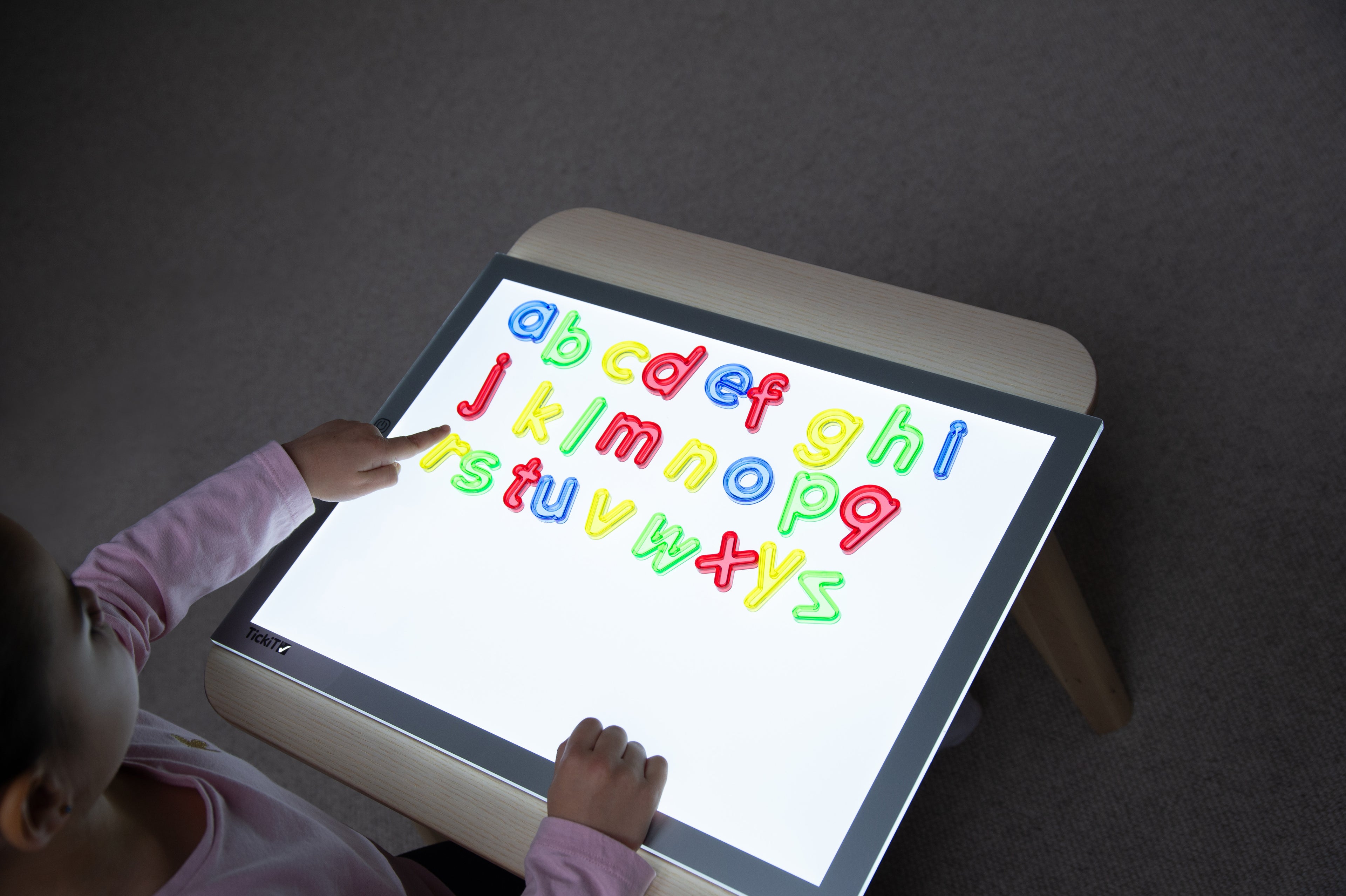 Translucent lowercase letters displayed on tablet screen with hands