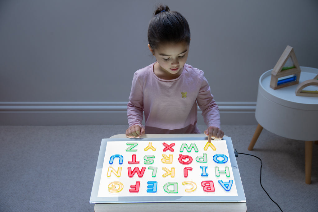 Translucent uppercase letter board with colorful A–Z letters, child reaching forward