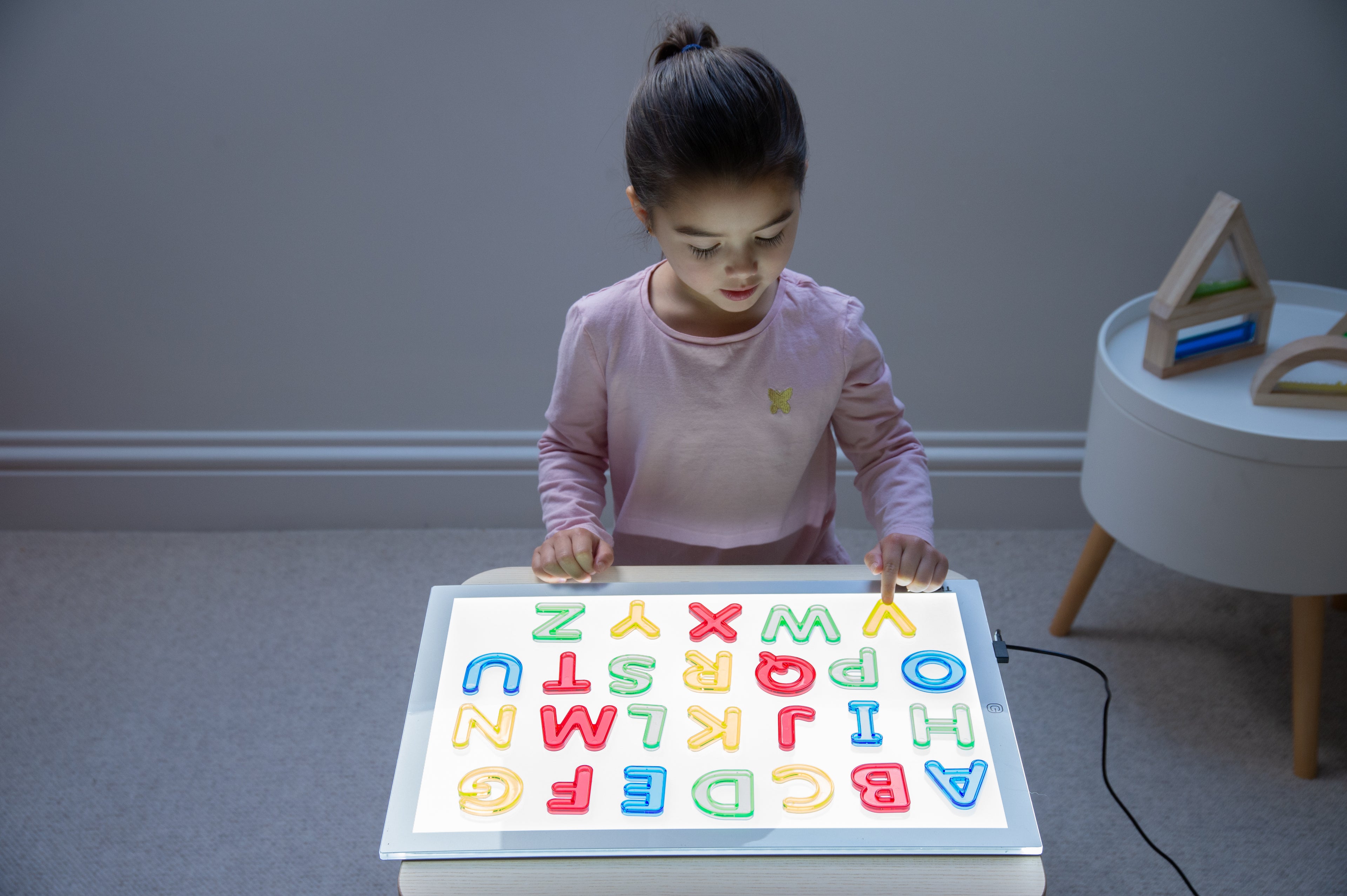 Translucent uppercase letter board with colorful A–Z letters, child reaching forward