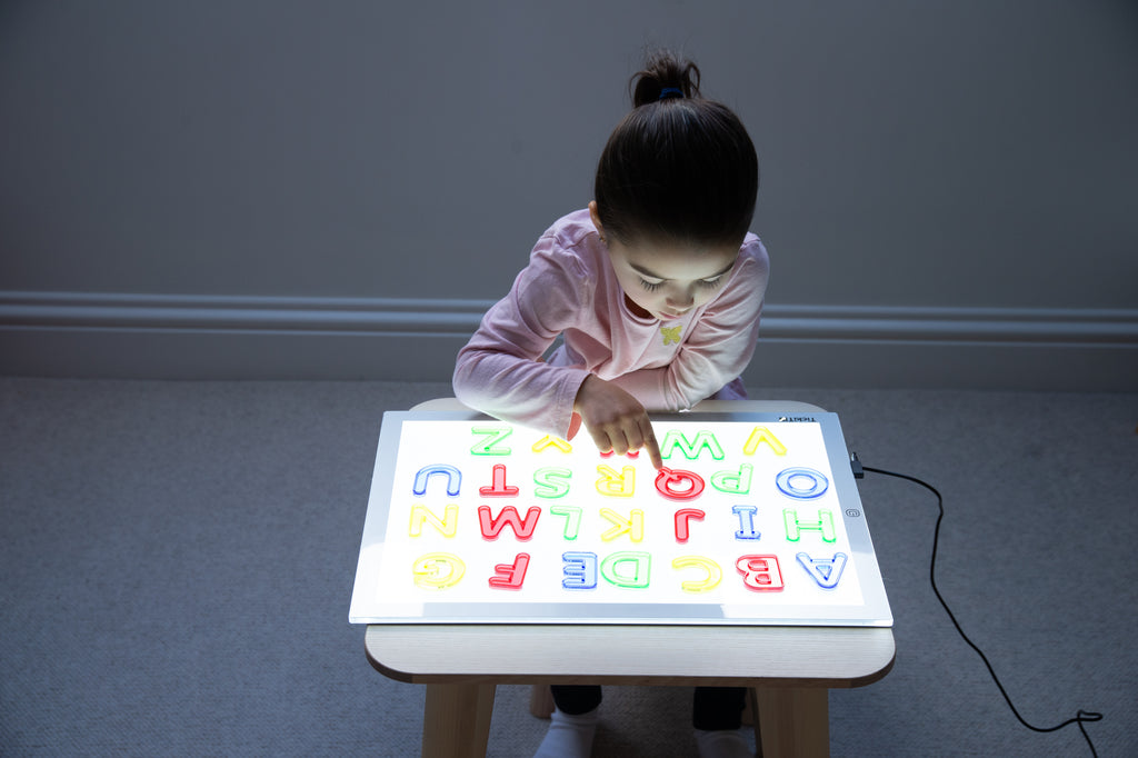 Translucent uppercase letter board with glowing A–Z letters, child playing at table