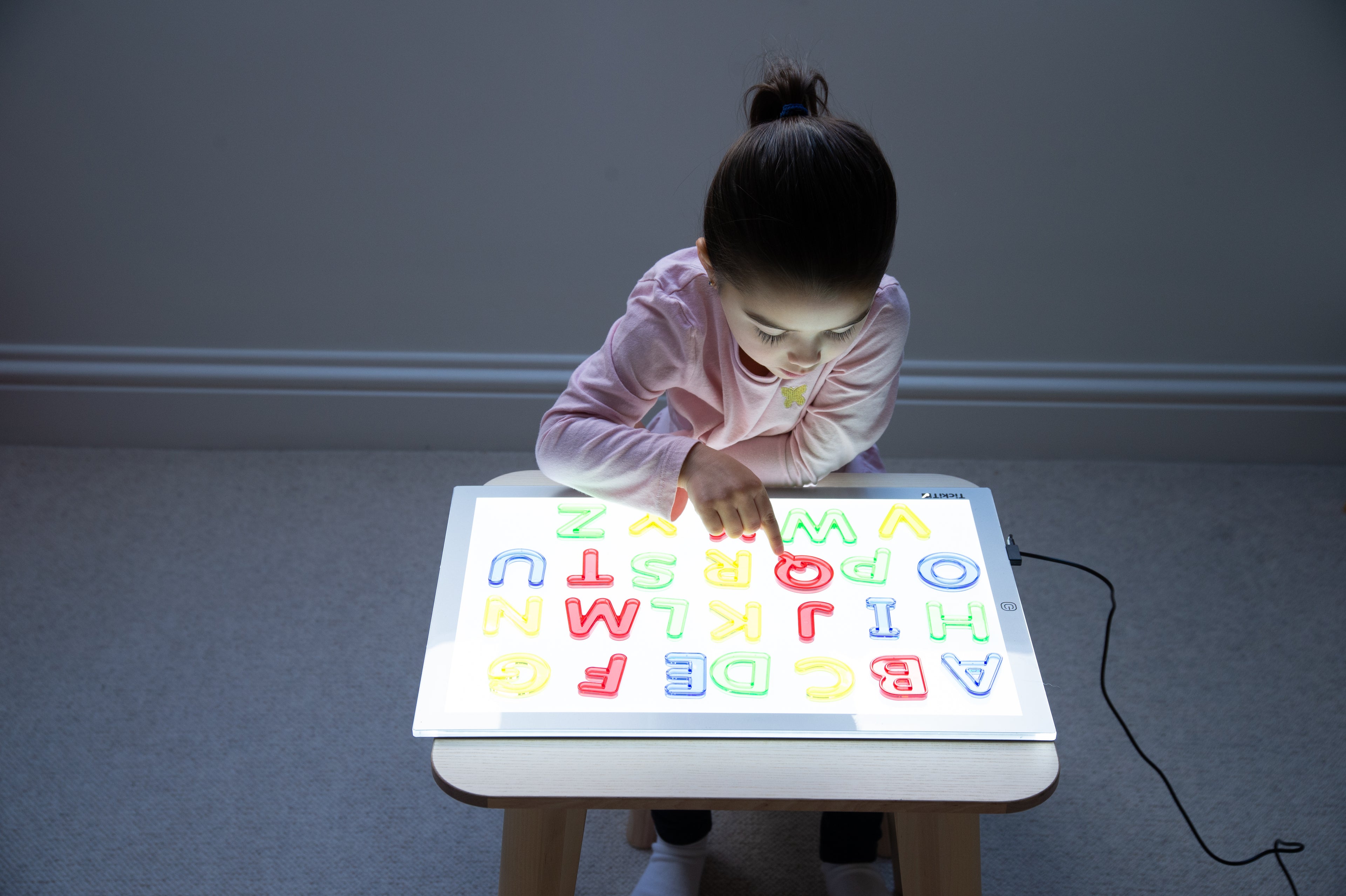 Translucent uppercase letter board with glowing A–Z letters, child playing at table