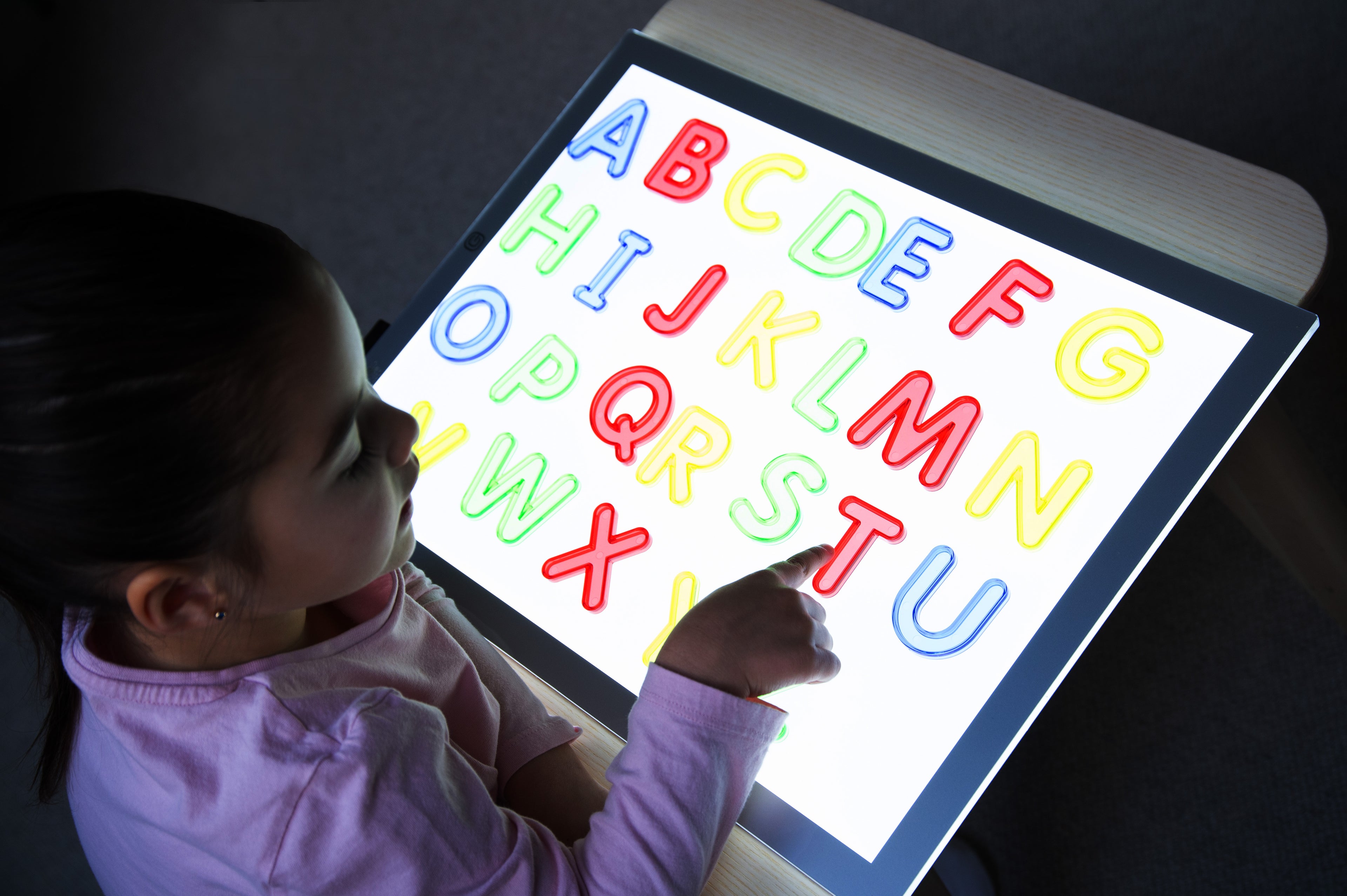 Translucent uppercase alphabet letters on glowing board, colorful A–Z with hands