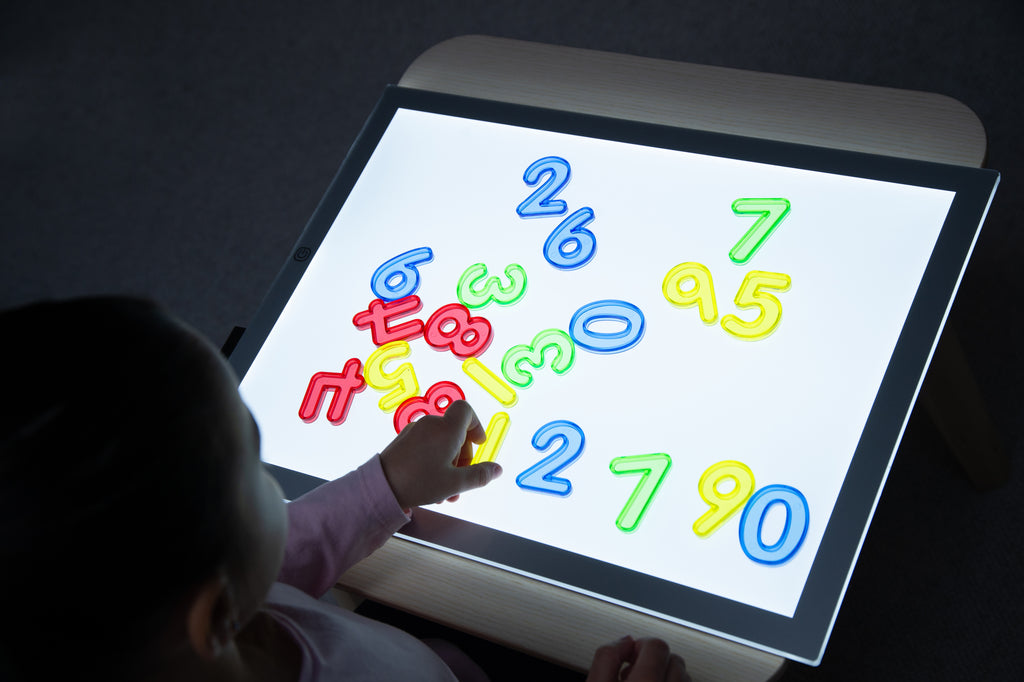 Kids using a backlit tablet with colorful translucent numbers displayed (0–9).