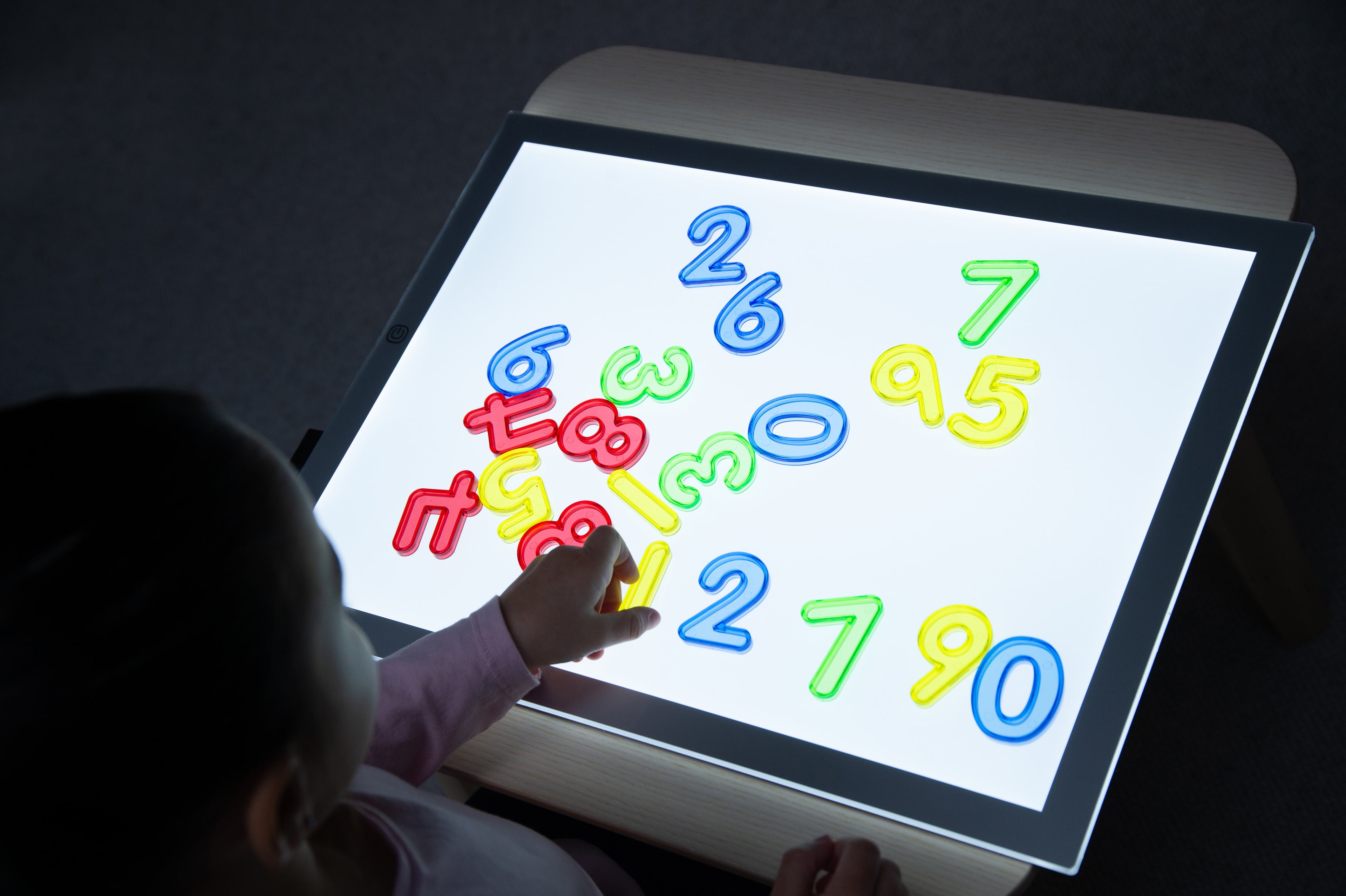 Kids using a backlit tablet with colorful translucent numbers displayed (0–9).