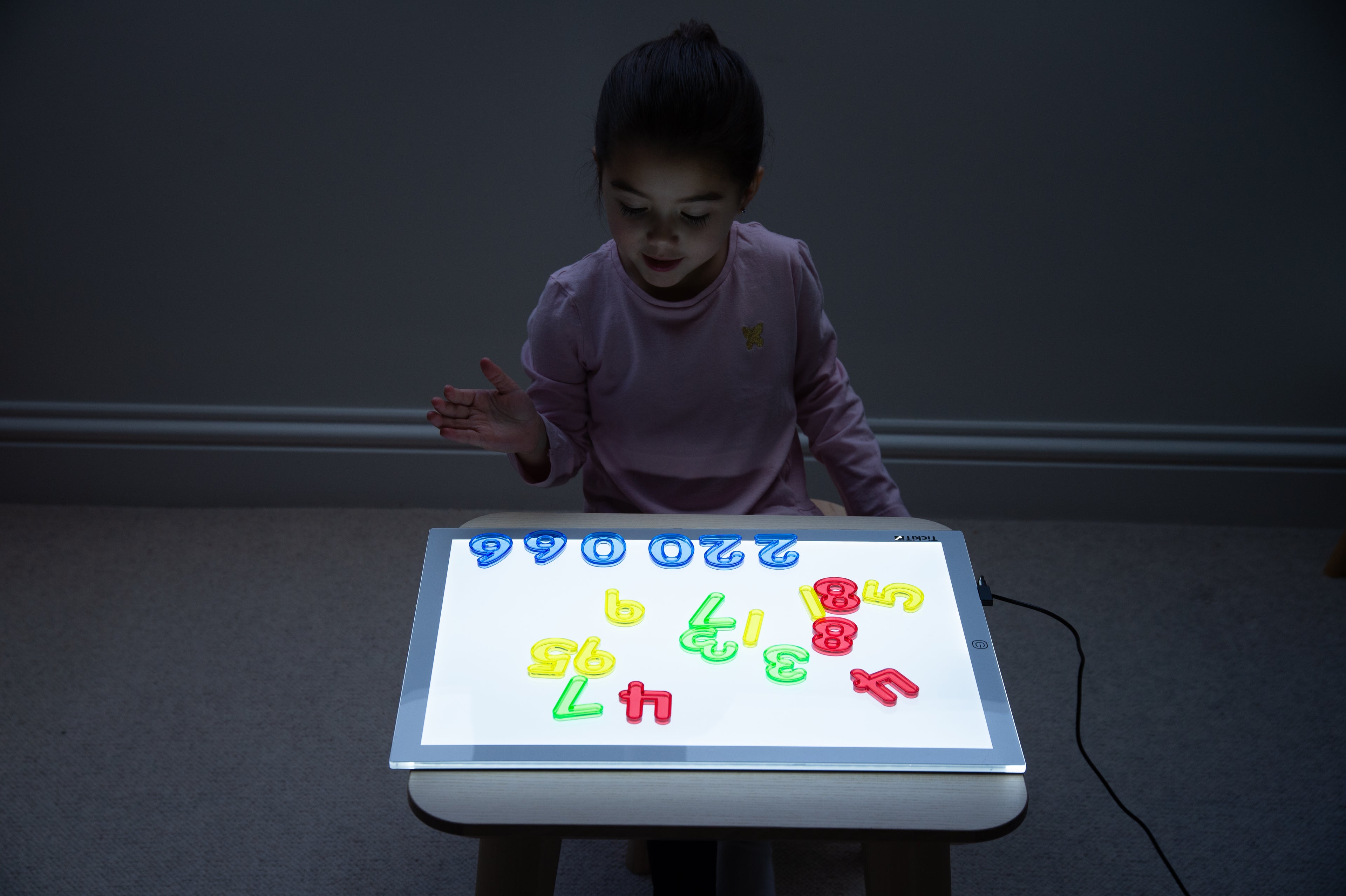 Child playing with a backlit number display tablet showing colorful translucent digits.